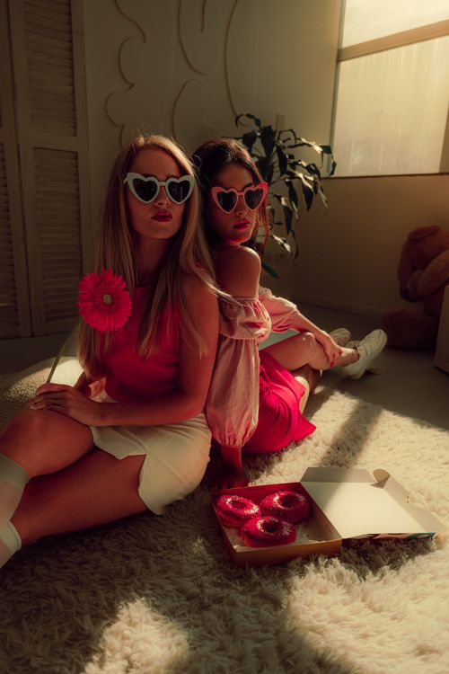 Free Two fashionable women with heart sunglasses enjoying donuts in a retro-themed room. Stock Photo