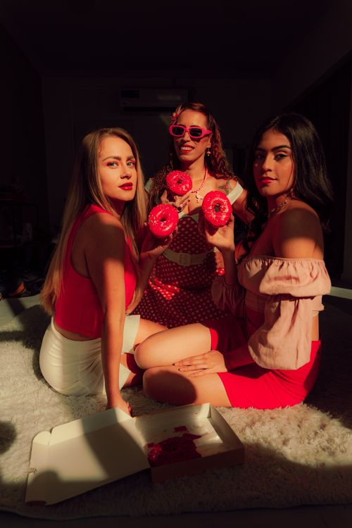 Free Three stylish young women enjoying donuts and sunshine indoors. Stock Photo