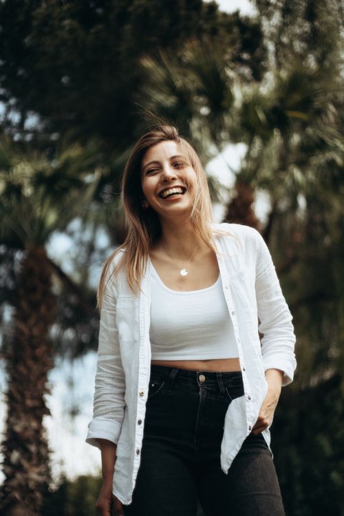 Free Smiling young woman enjoying a sunny day outdoors with palm trees. Stock Photo