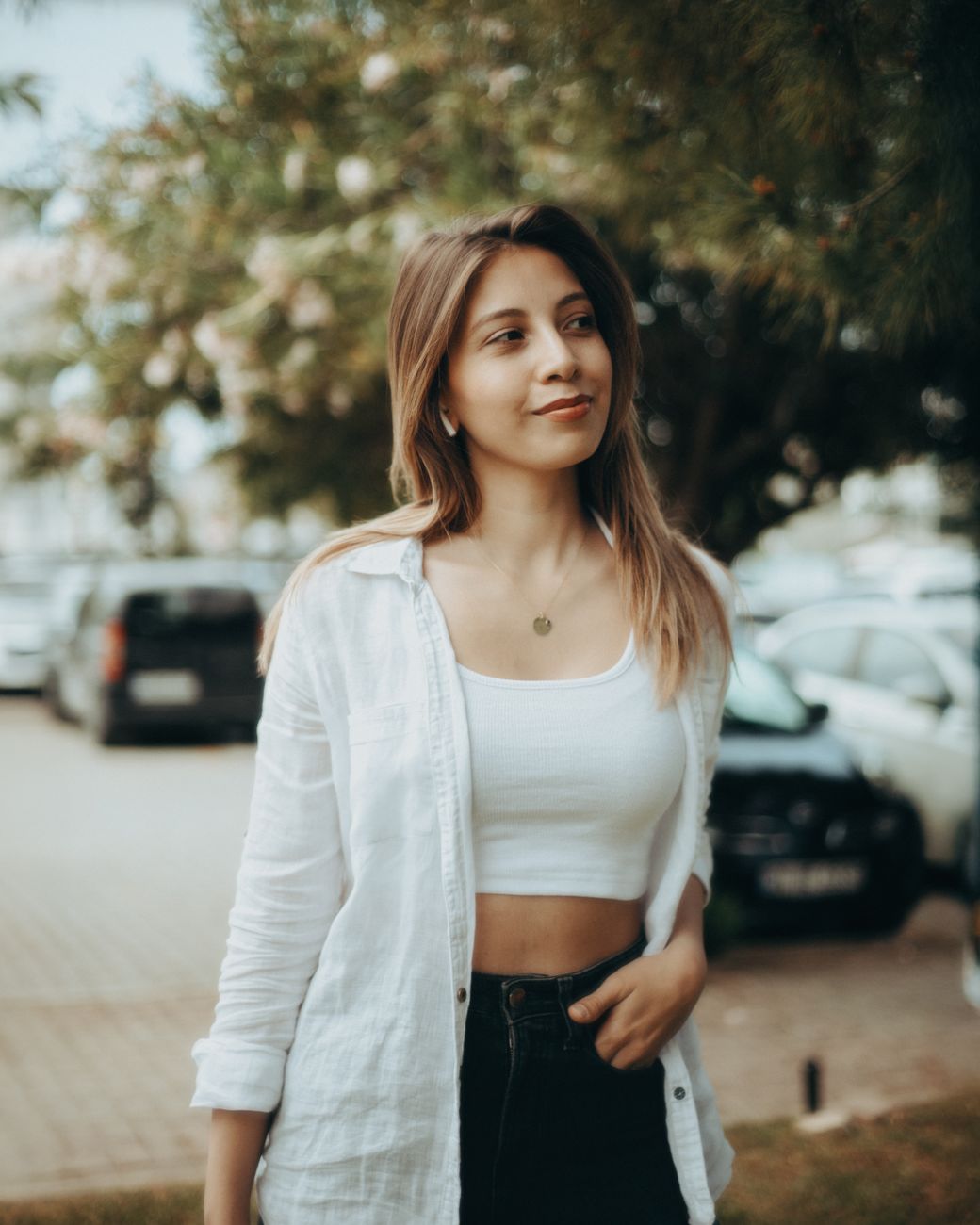 Young woman in casual outdoor setting wearing white top and shirt, relaxed and smiling.