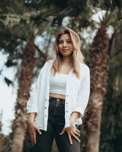 Free A young woman stands confidently among palm trees on a sunny day, exuding a relaxed vibe. Stock Photo
