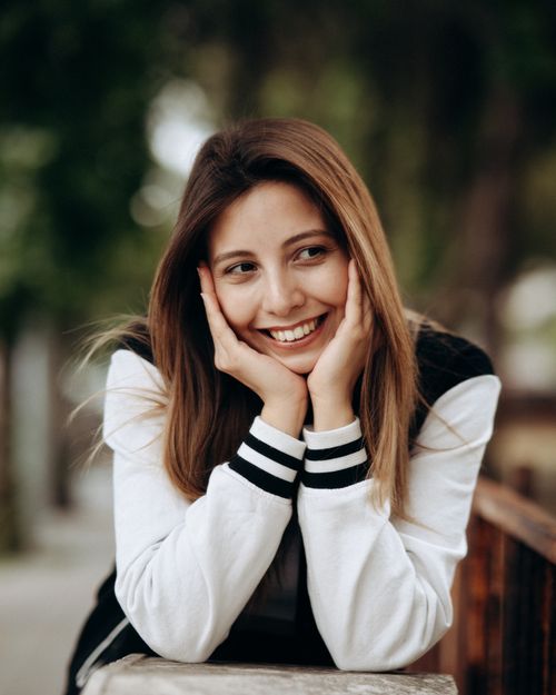 Free A young woman leaning on a railing, smiling warmly outdoors. Stock Photo