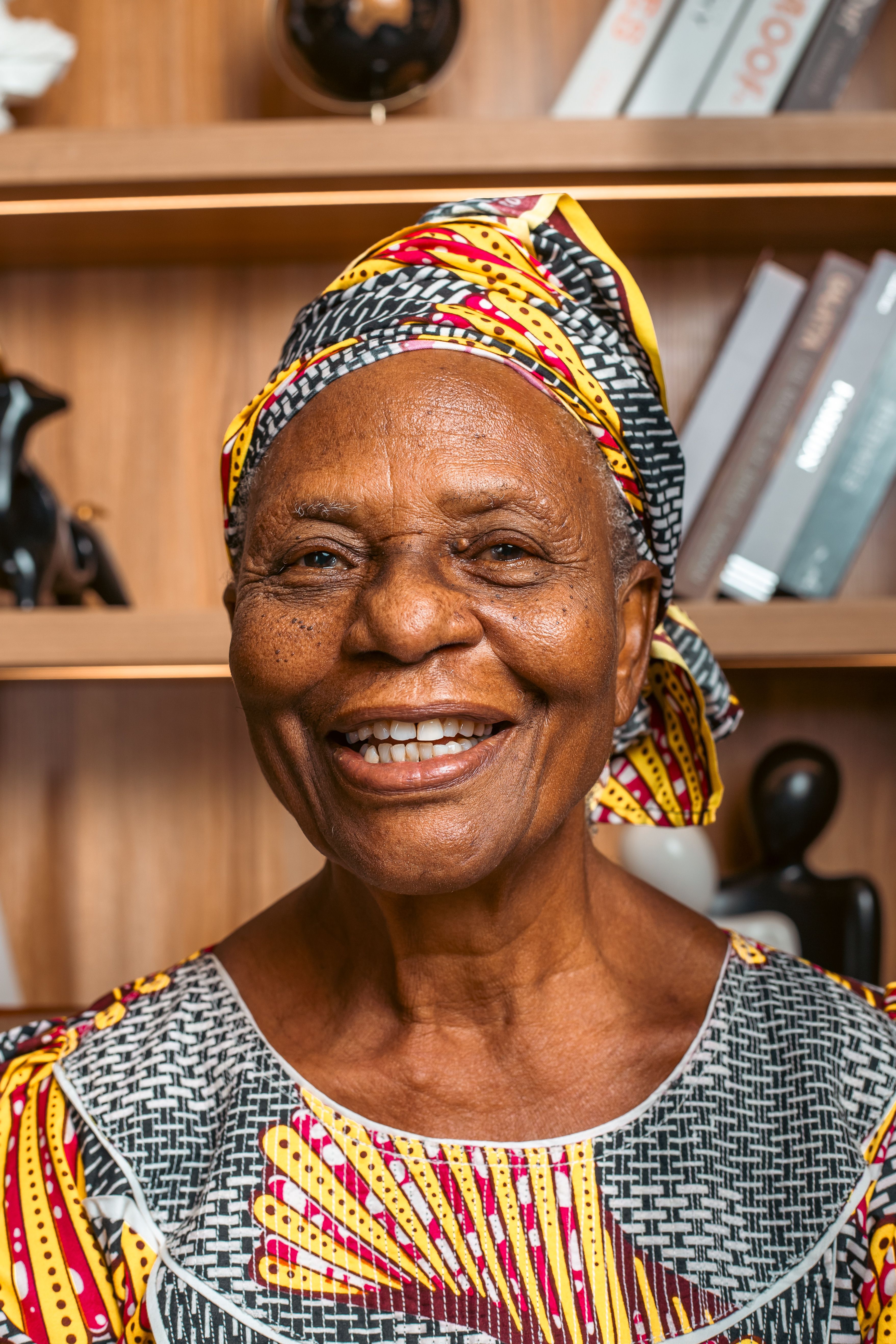 Joyful senior woman wearing vibrant African print clothing, smiling warmly indoors.