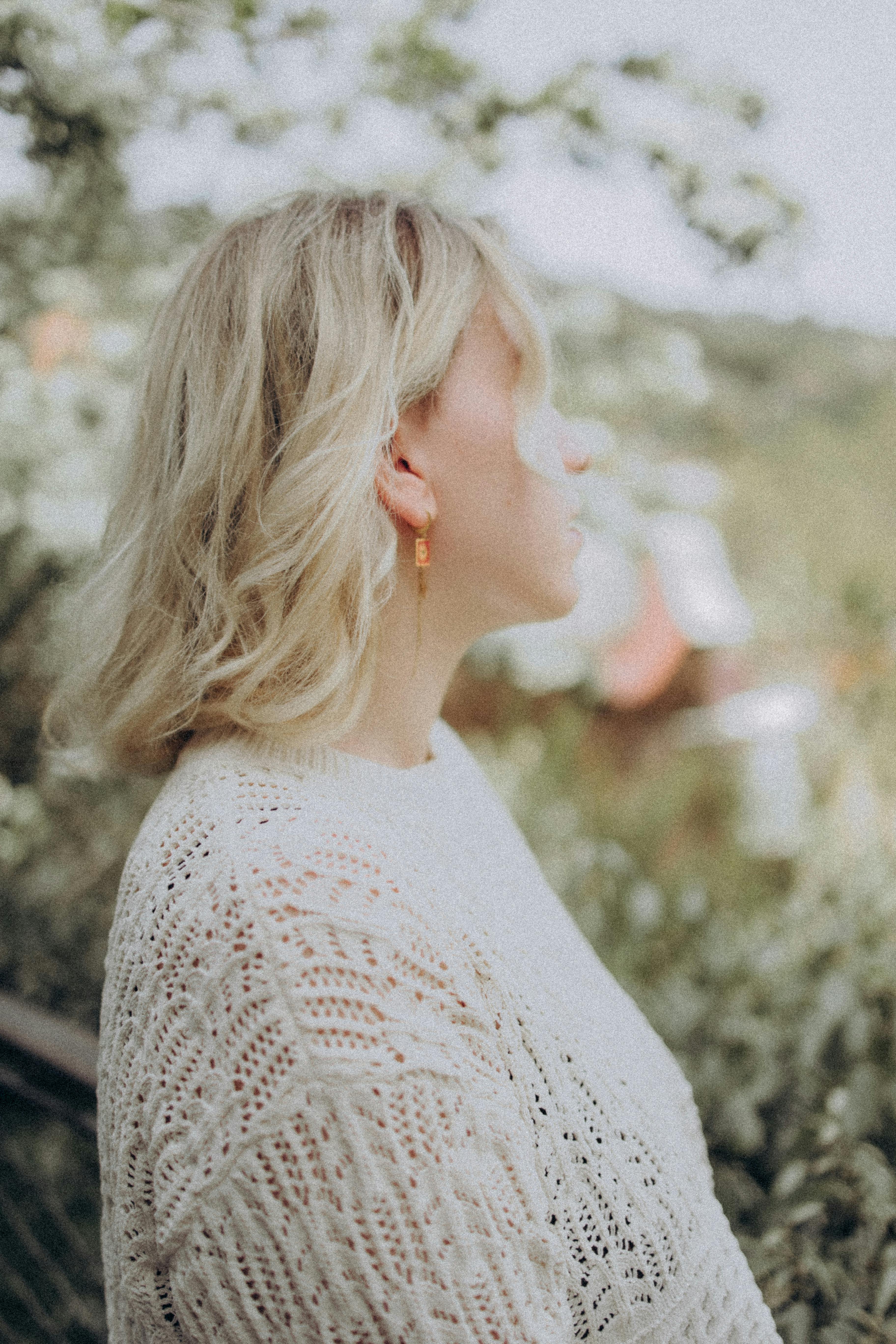 Side profile of a woman in a lace sweater enjoying nature outdoors.