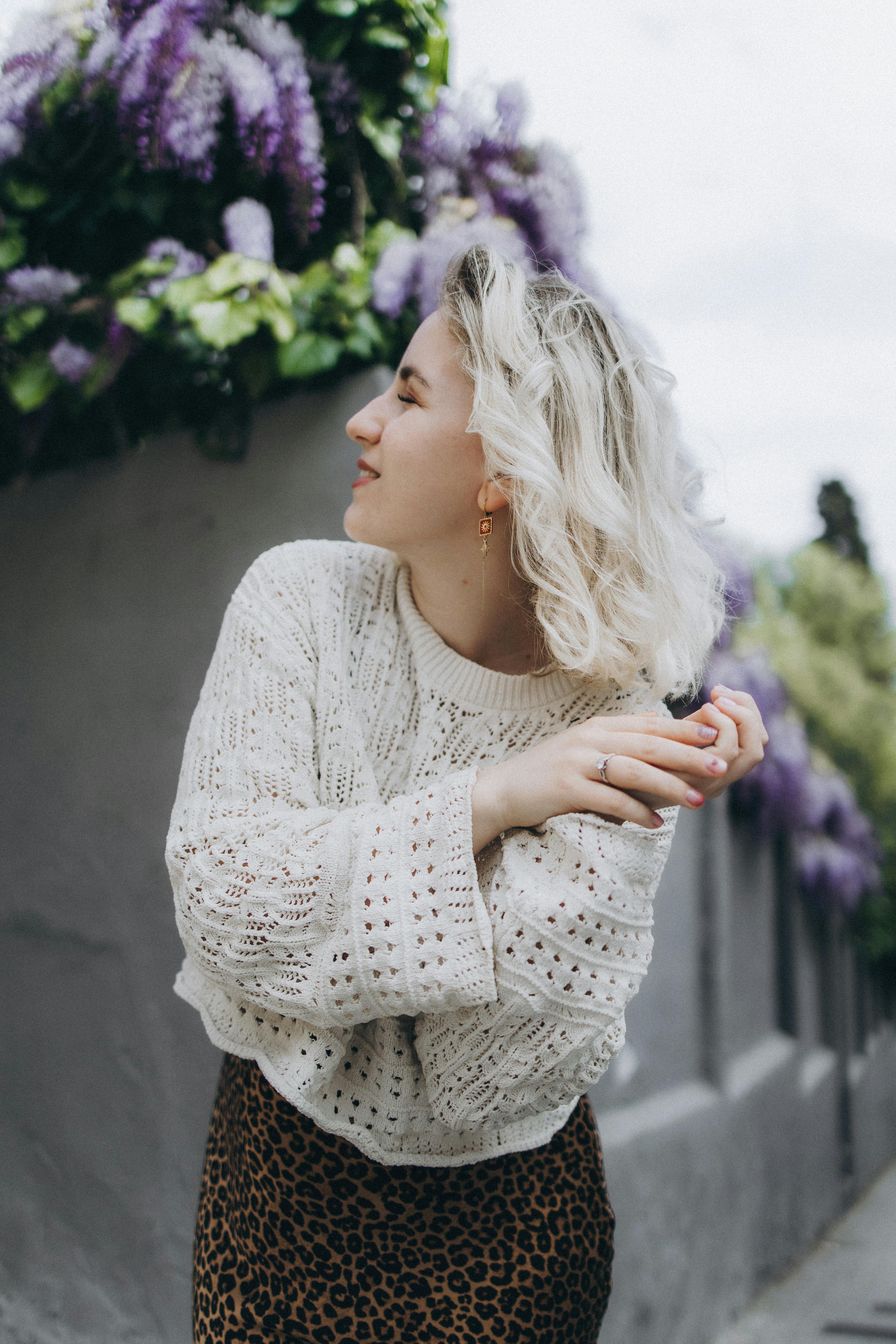 Stylish woman in knitted sweater enjoying a vibrant outdoor setting with blooms.