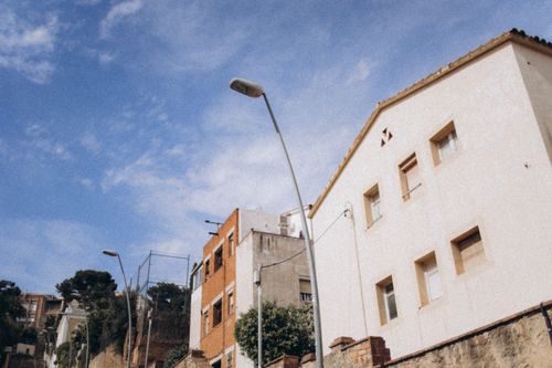 Free Captivating street view of urban residential buildings against a clear blue sky, featuring lampposts and greenery. Stock Photo