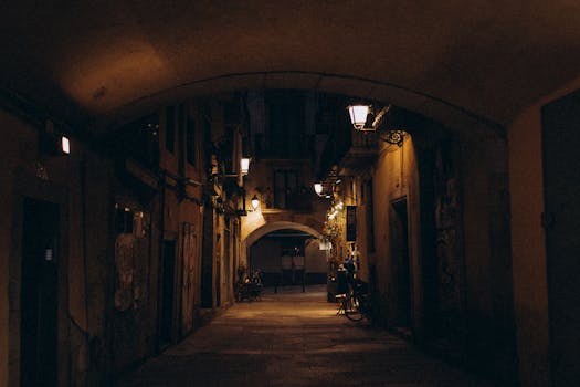 A dimly lit, atmospheric alley at night with arched architecture and warm street lighting.