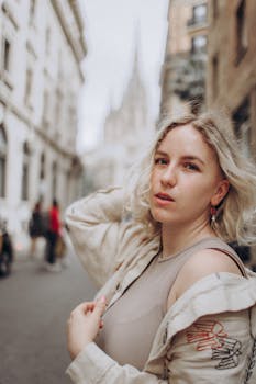 Blonde woman poses in city street with blurred cathedral backdrop.
