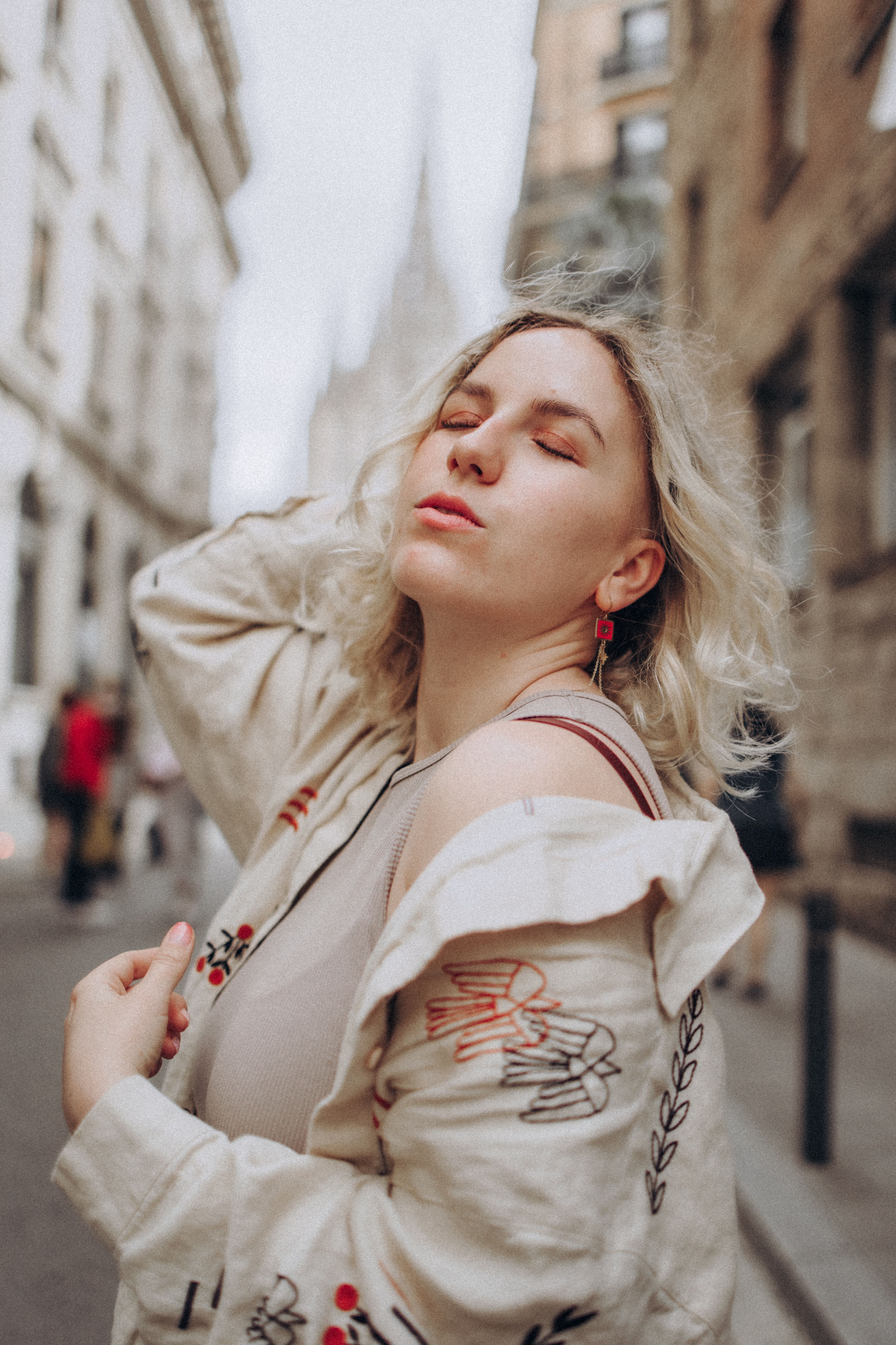 A woman stands serenely on a city street, eyes closed and embracing the moment.