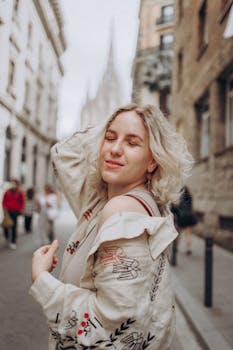 A cheerful woman with blonde hair enjoys a sunny day on a European city street.