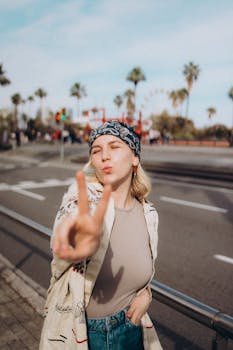 Smiling young woman showing peace sign outdoors with a Ferris wheel in the background.