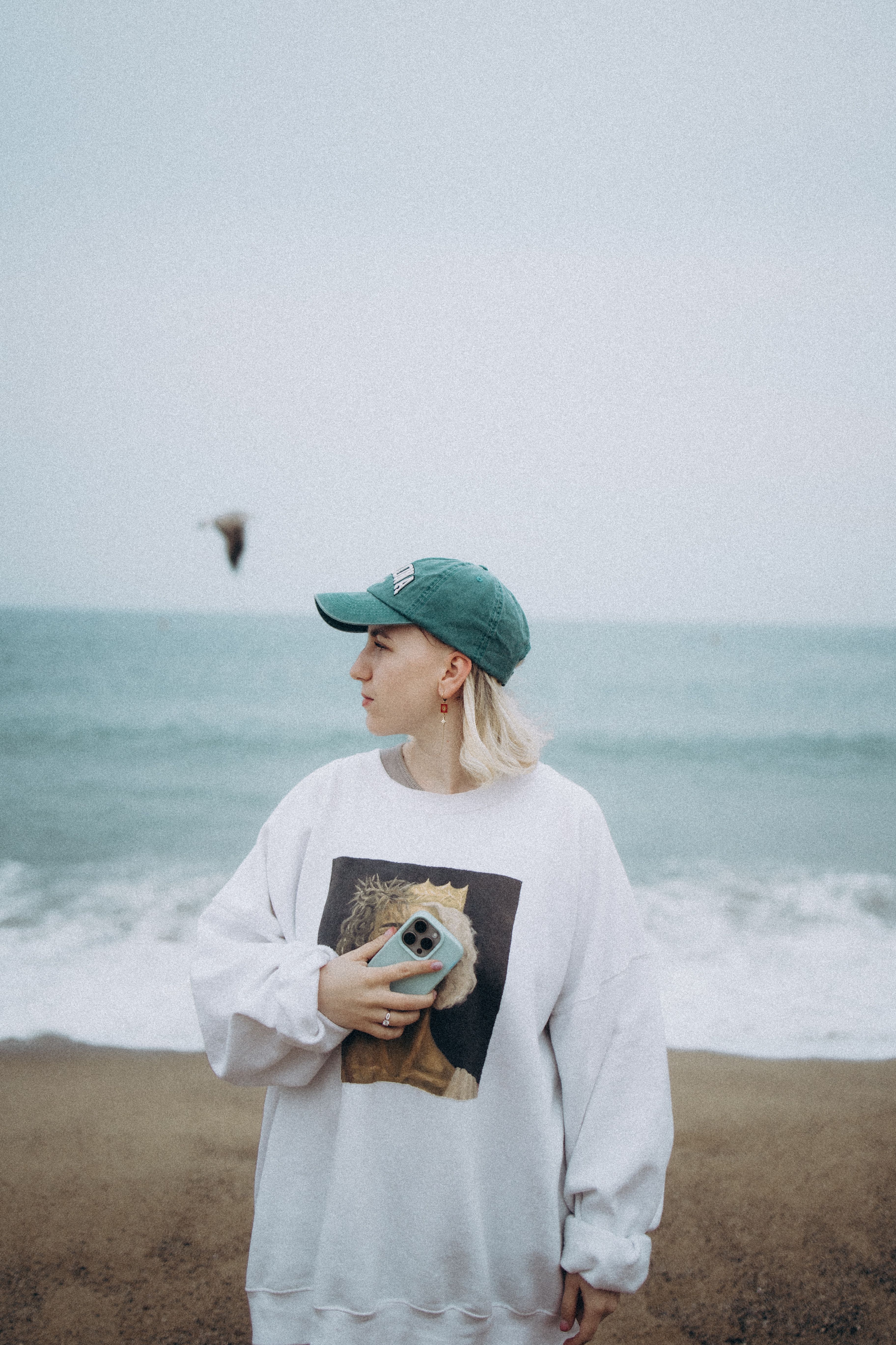 Young woman with a phone by the sea, donning casual urban attire at a beach in Barcelona, Spain.