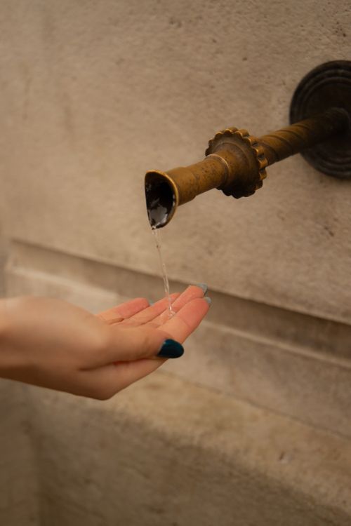 Free A close-up shot of a hand catching water from an ornate antique fountain spout outdoors. Stock Photo
