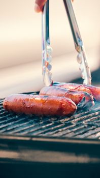 Juicy sausages sizzling on a barbecue grill with tongs, perfect for a summer cookout.