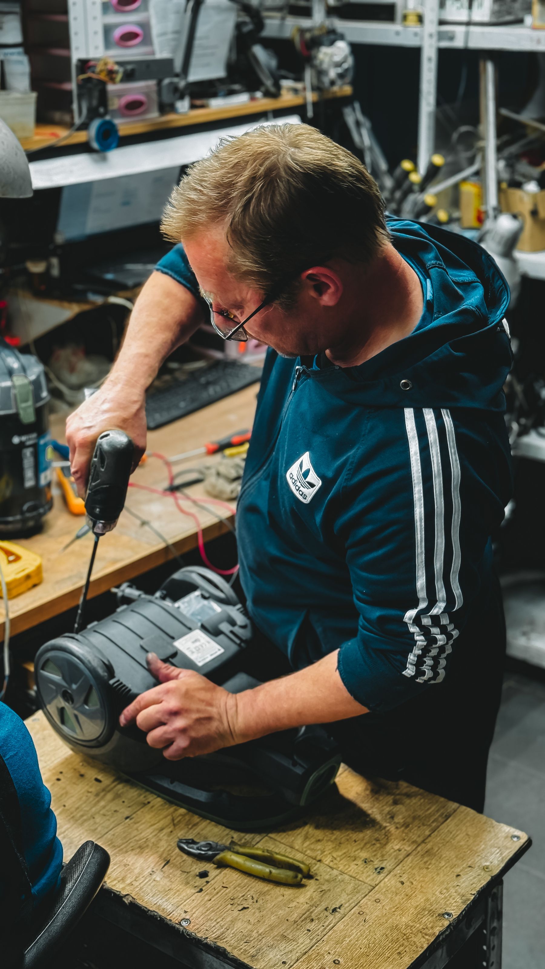 Technician using a cordless drill to repair workshop equipment on a wooden workbench