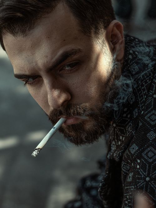Free Dramatic portrait of a man smoking with intense gaze, dark setting. Stock Photo
