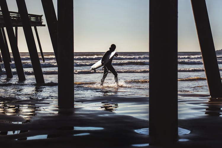 Surfer Walks Near Dock At The Beach