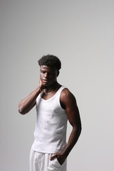 Thoughtful young man in white tank top posing against a neutral background.
