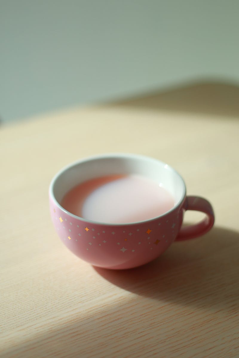 A pastel pink teacup with a blush drink on a light wooden table, evoking a soft cozy cafe aesthetic