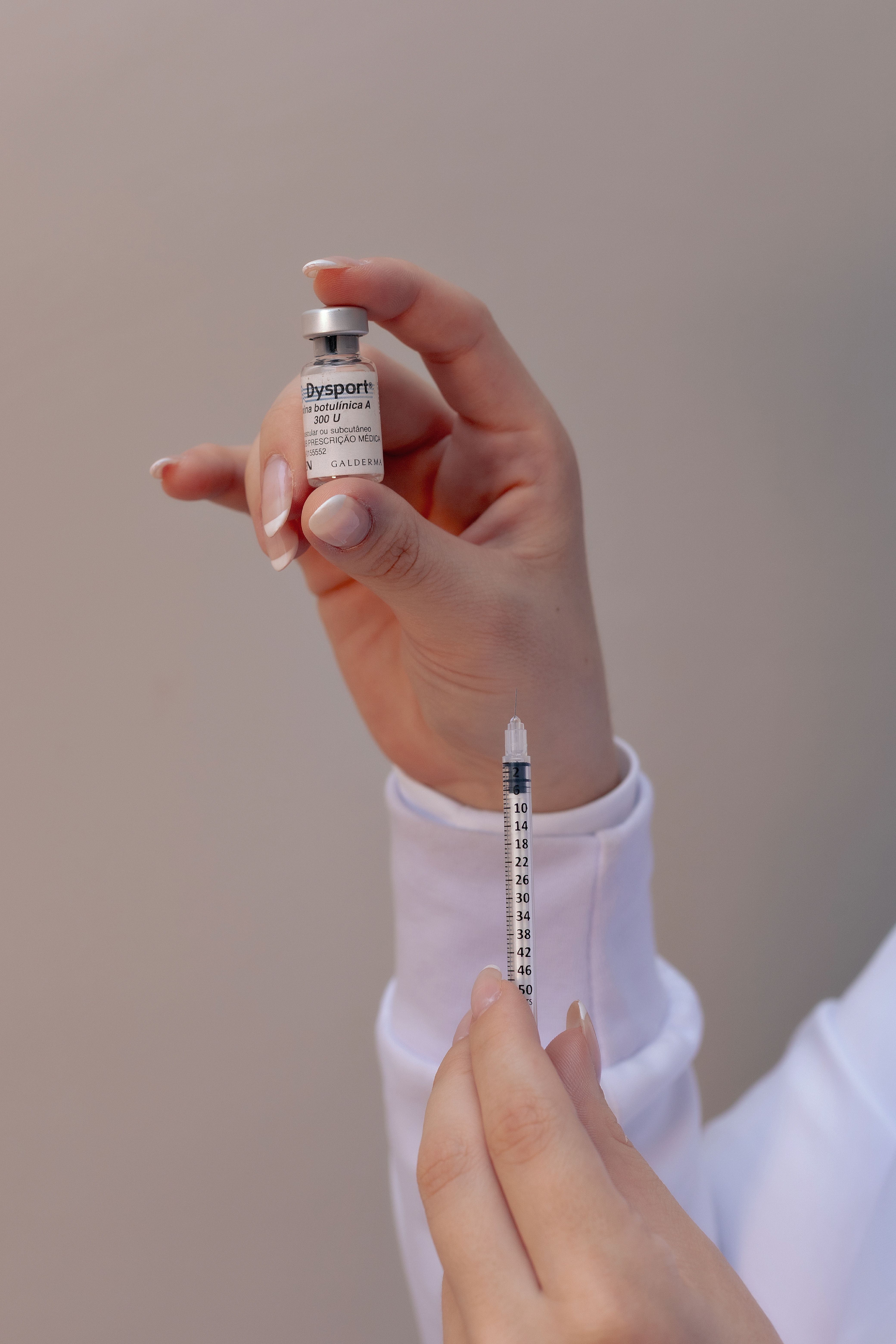 A close-up of hands holding a cosmetic injection and vial, ready for application.