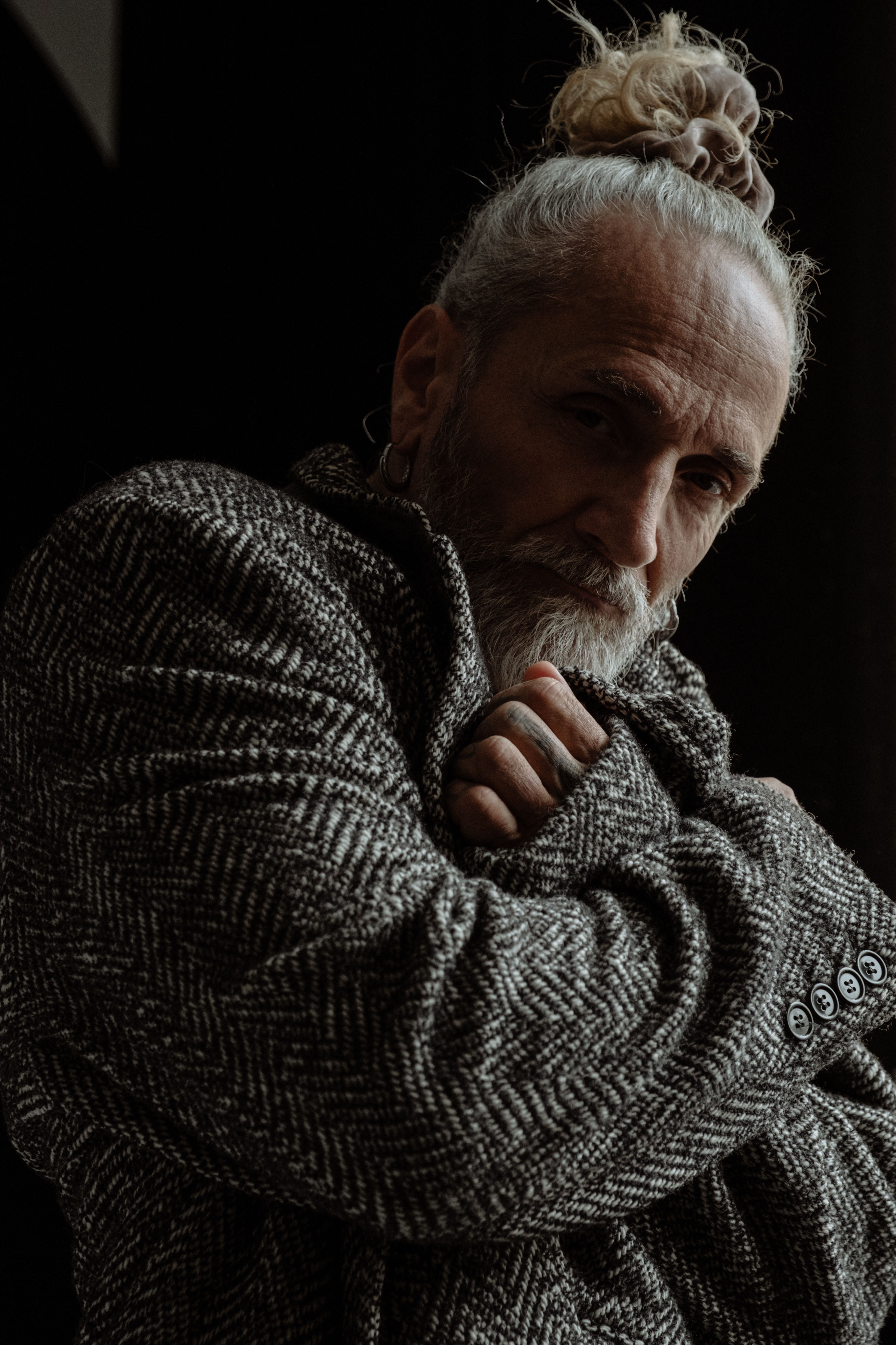 Moody portrait of a senior man with a unique hairstyle wearing a tweed coat.