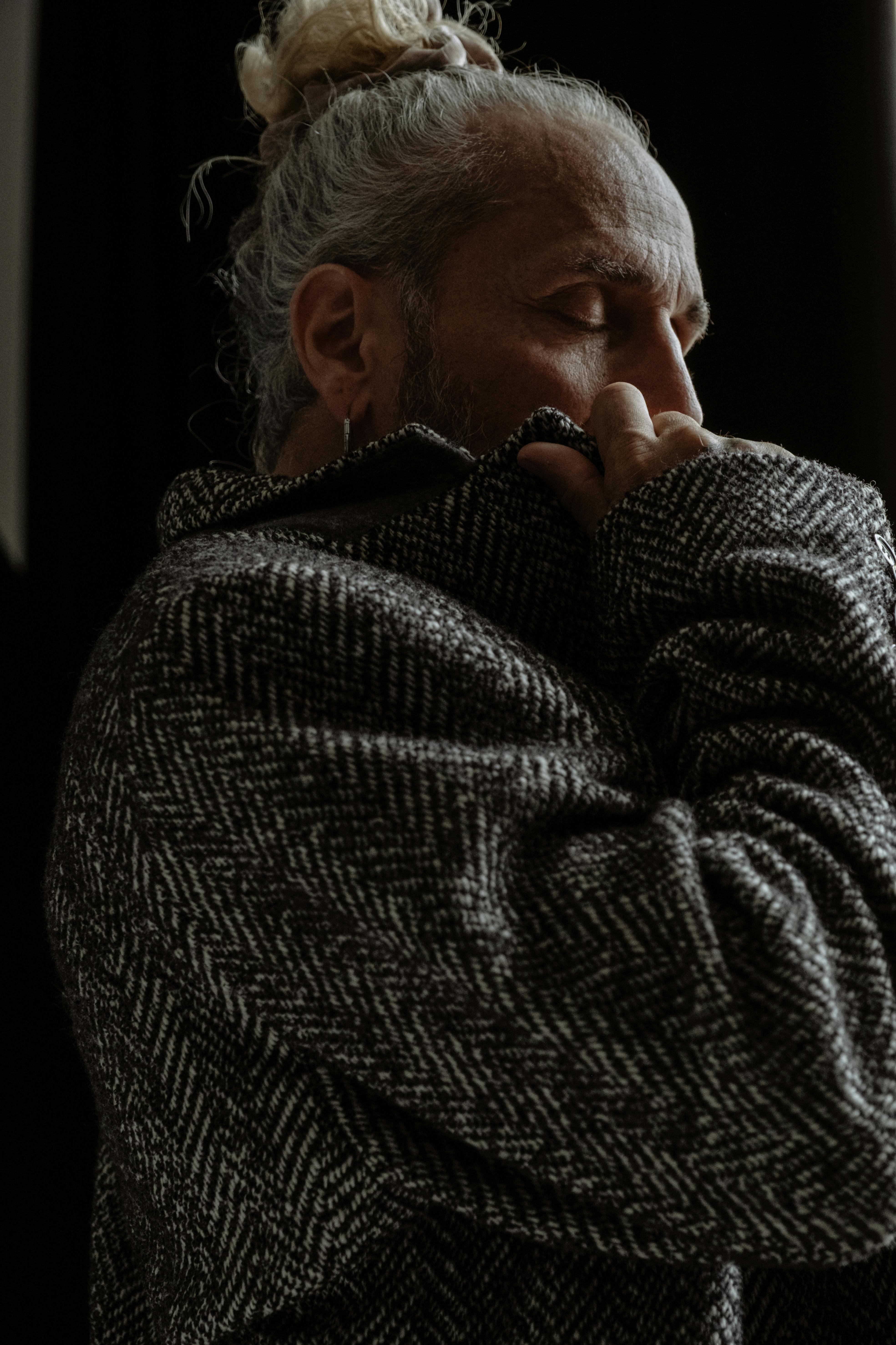 Elderly man with gray hair in a dimly lit room wearing a textured sweater.