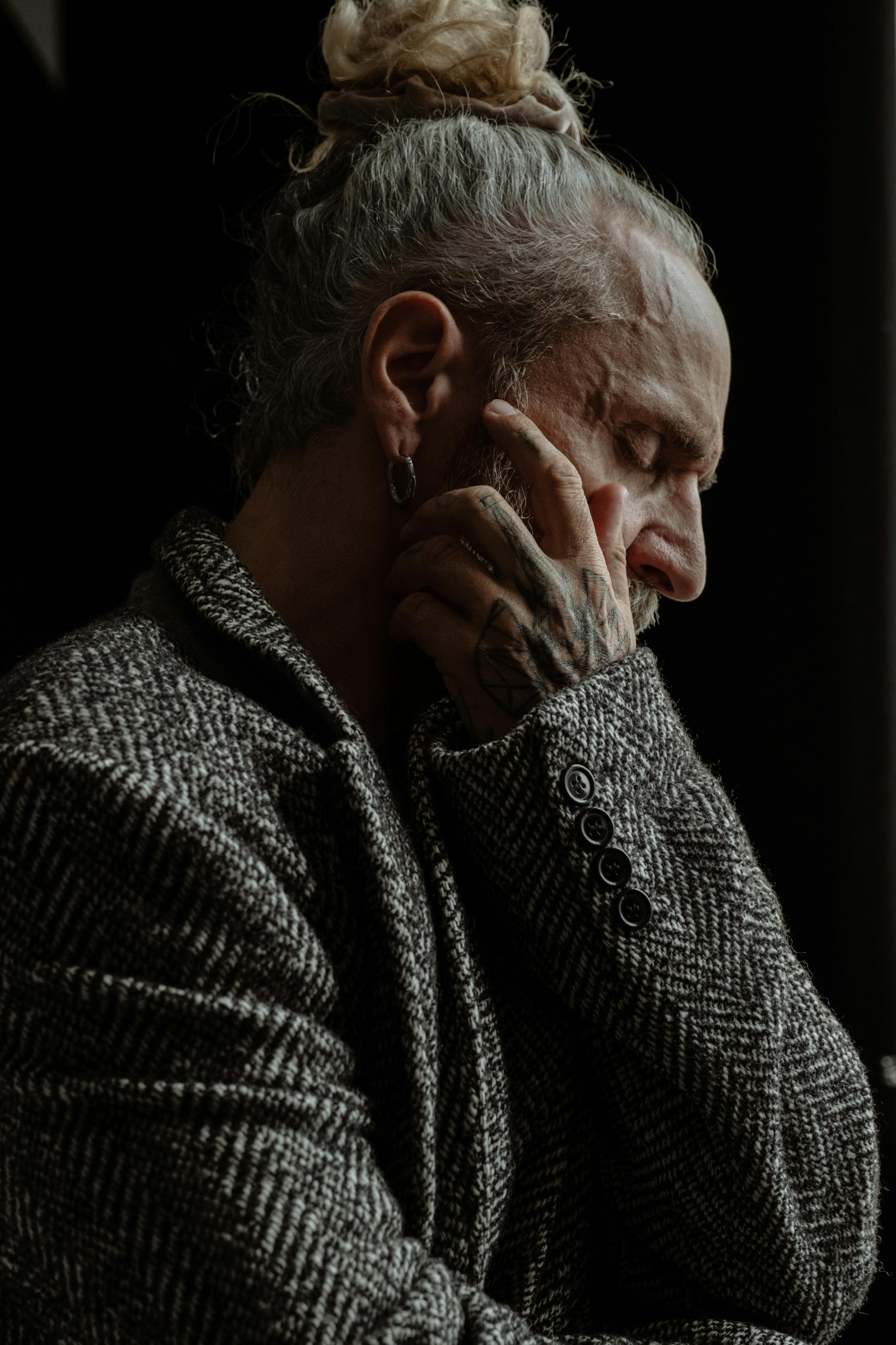 A thoughtful tattooed man in a textured coat, captured in moody lighting and deep contemplation.