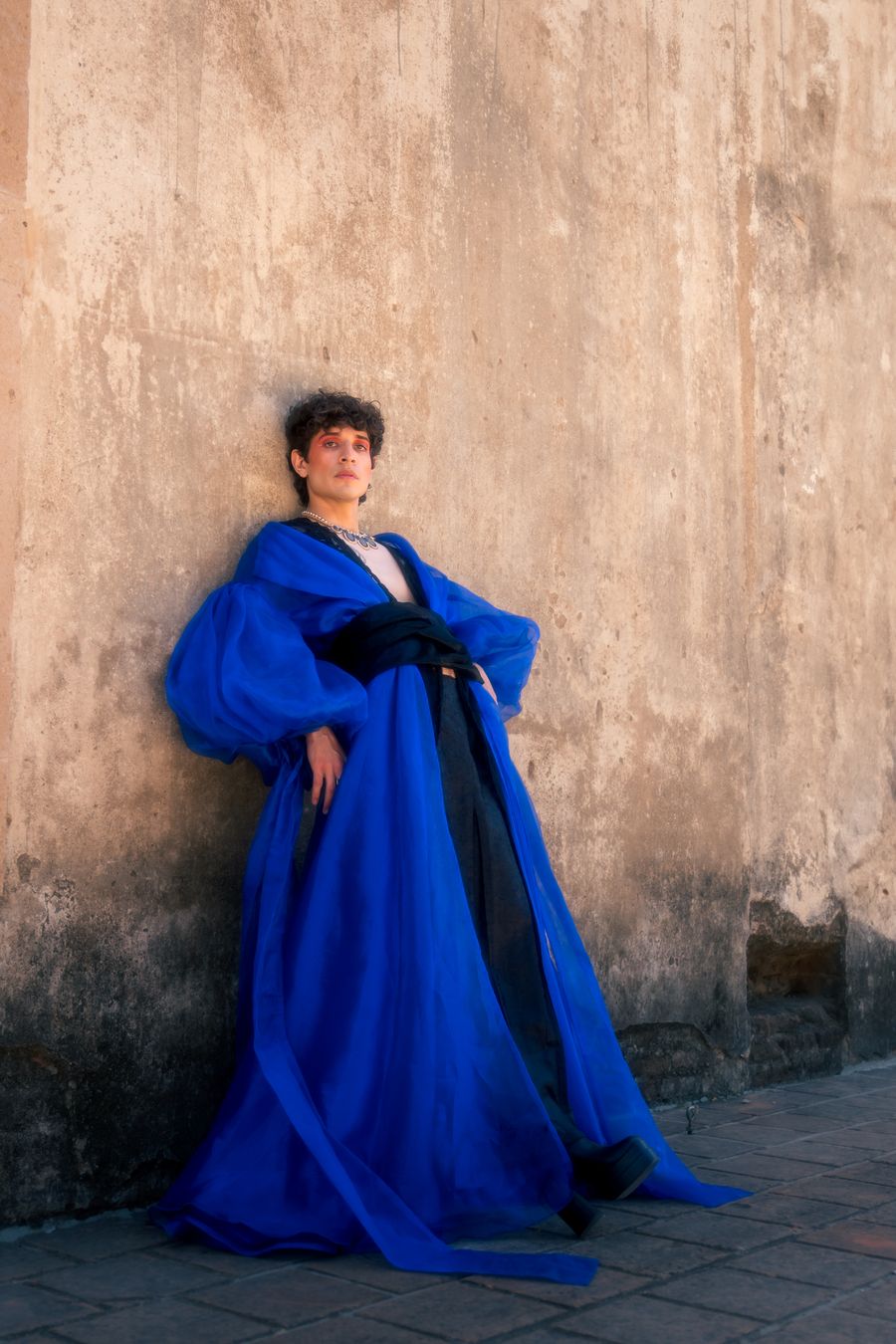 Model in a cobalt blue gown against a weathered wall