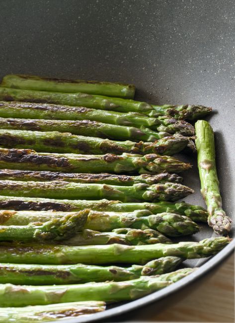 A sheet pan of roasted asparagus spears with lightly charred tips and a wedge of lemon on the side.