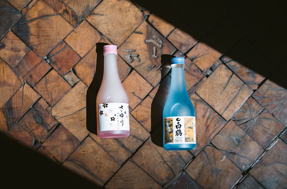 Two sake bottles in pink and blue casting shadows on a wooden floor.