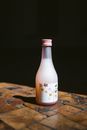 Pink capped sake bottle with floral label on a wooden surface, highlighted by natural light.