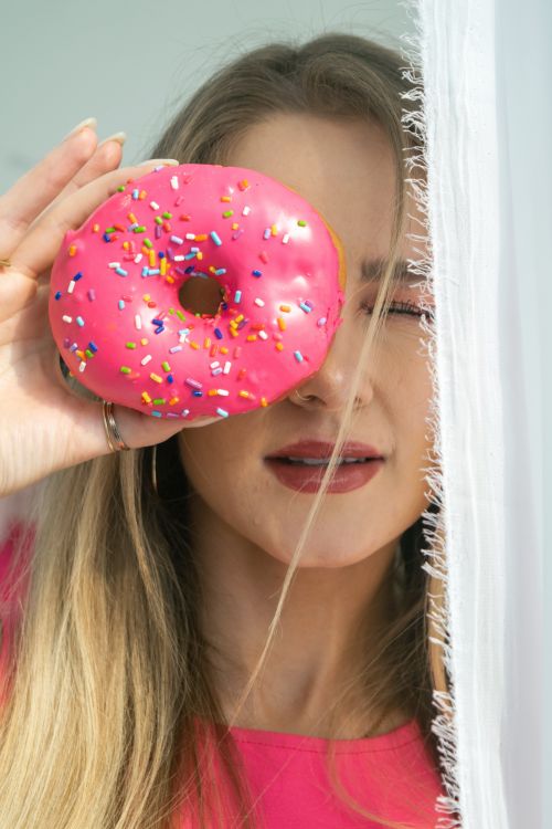 Free Woman playfully holding a pink sprinkled doughnut over her eye. Stock Photo