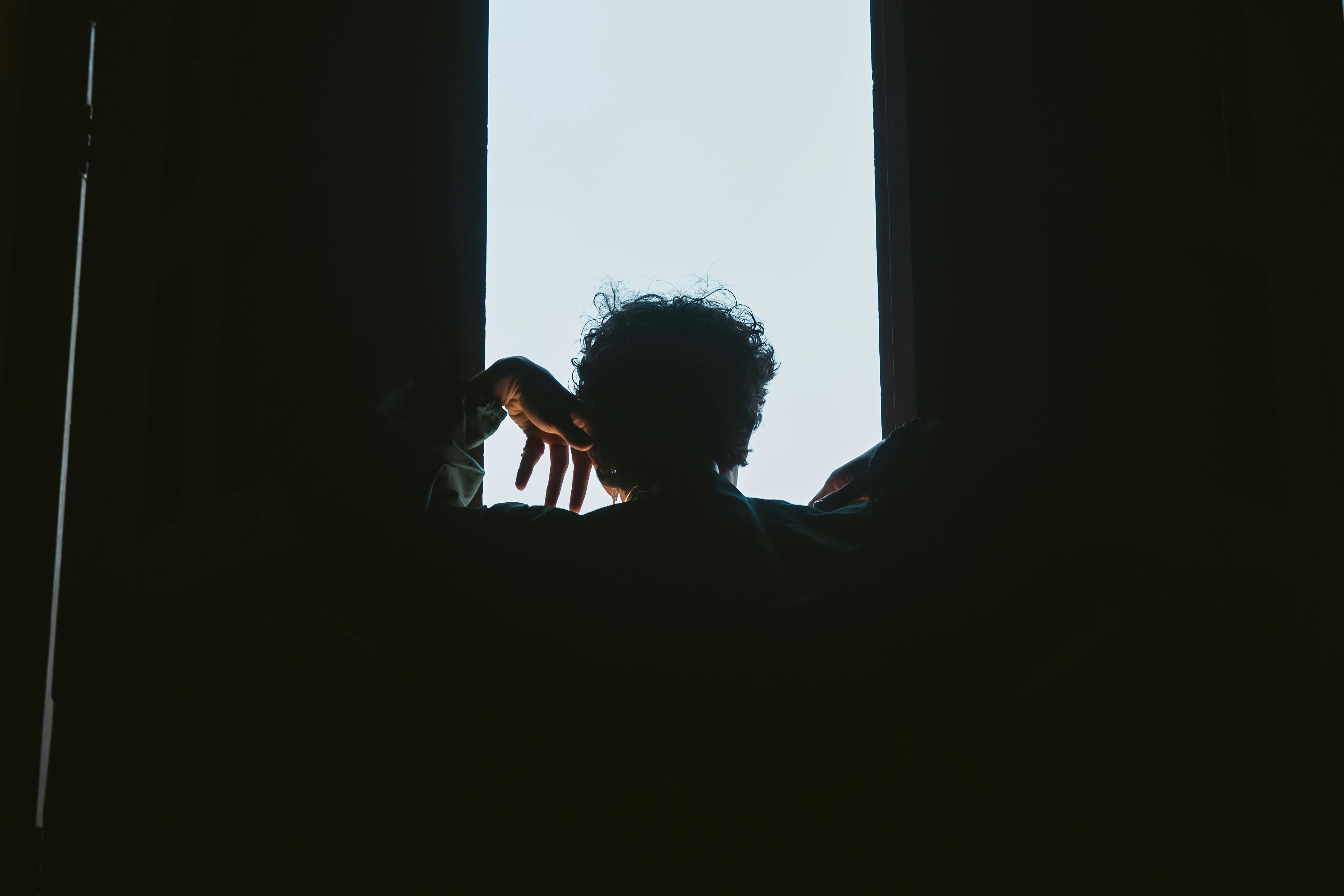 A person silhouetted against a bright window, creating a dramatic contrast between light and shadow.