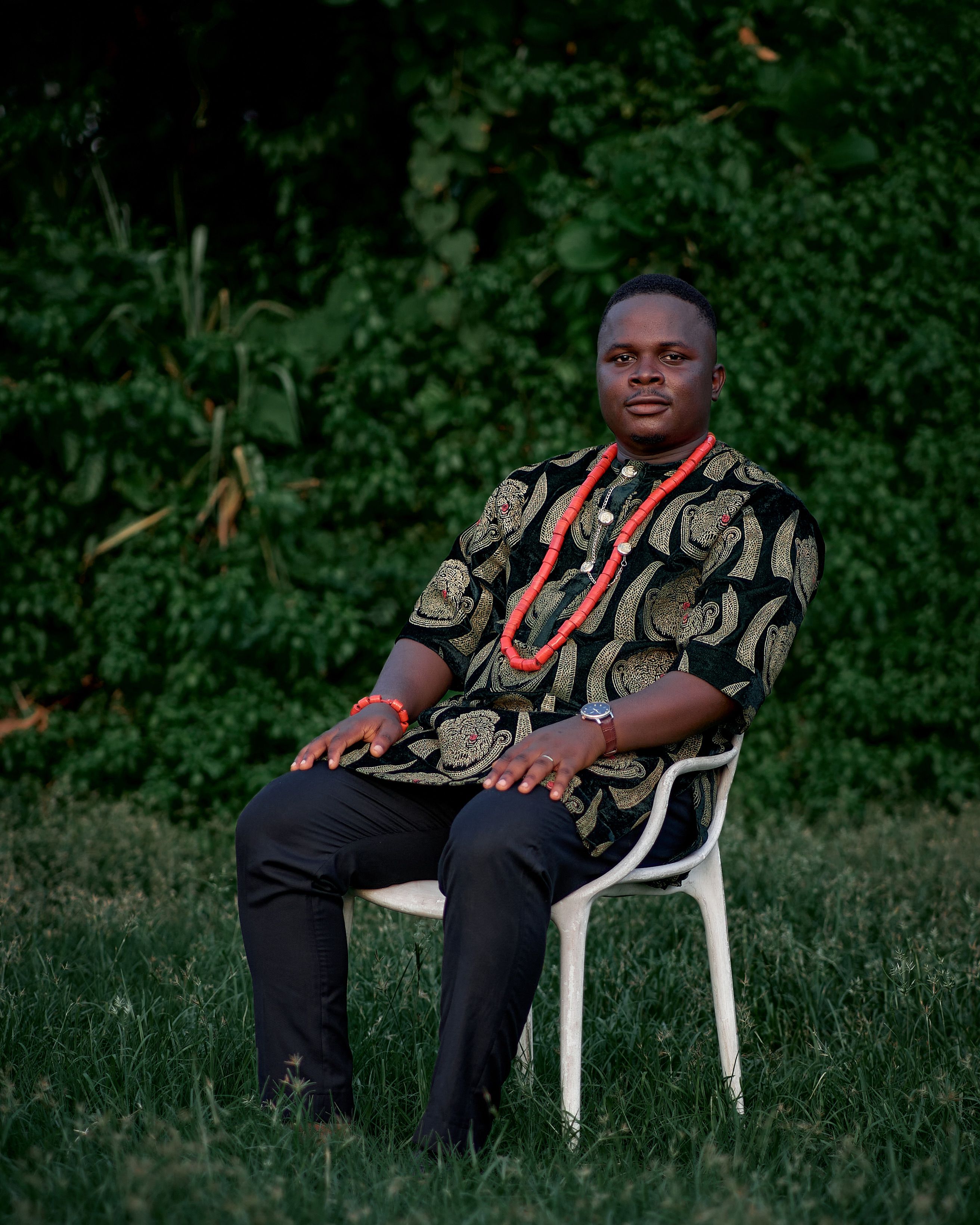 Portrait of an adult male in traditional clothing seated on a chair outdoors.