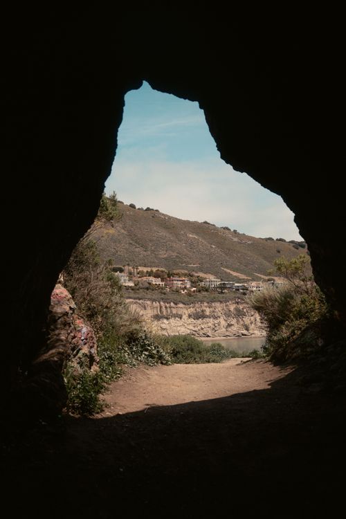 Free A cave opening provides a natural frame for a stunning mountain view under a clear blue sky. Stock Photo