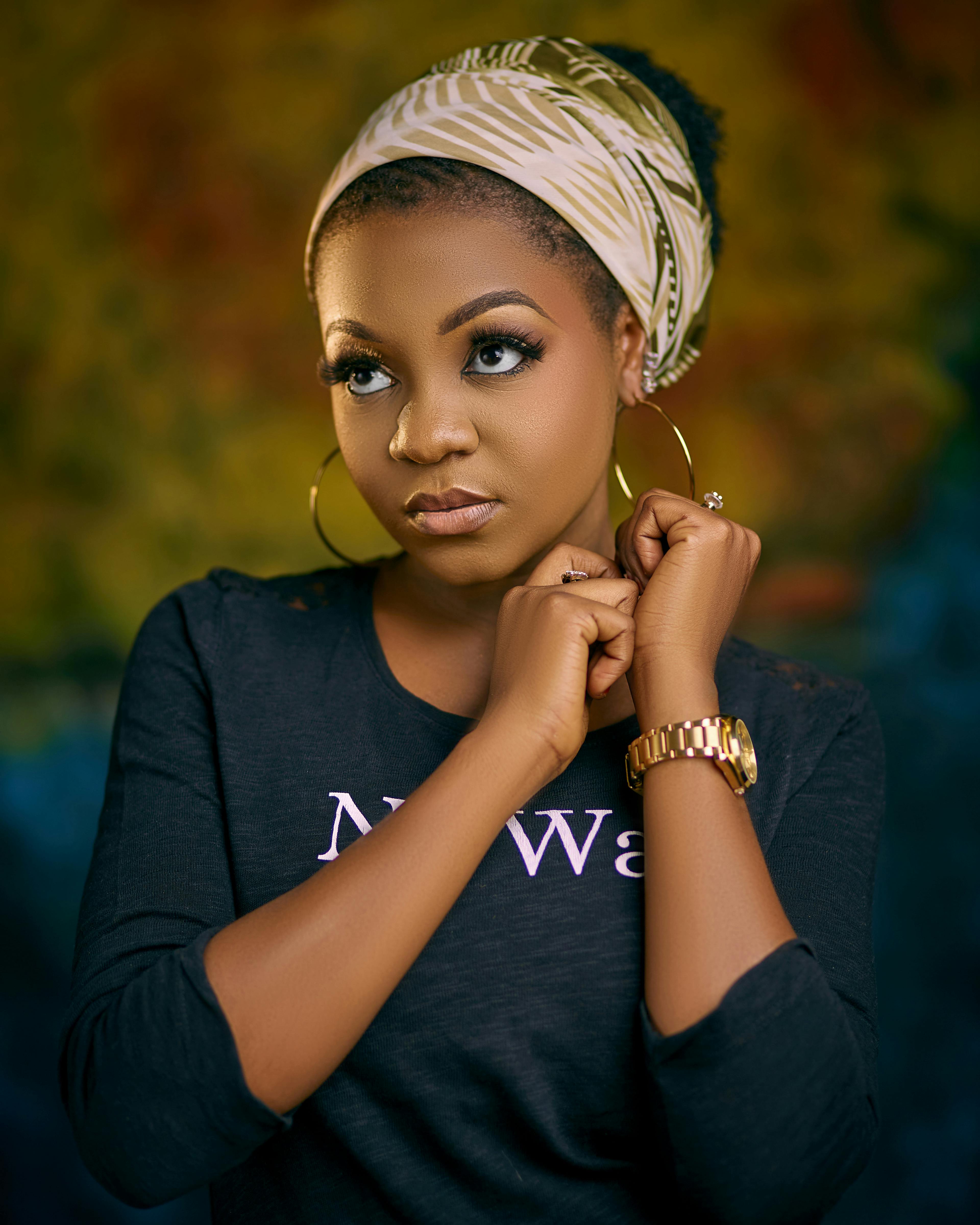 Sophisticated woman posing in black shirt with headscarf and gold watch against a blurred background.