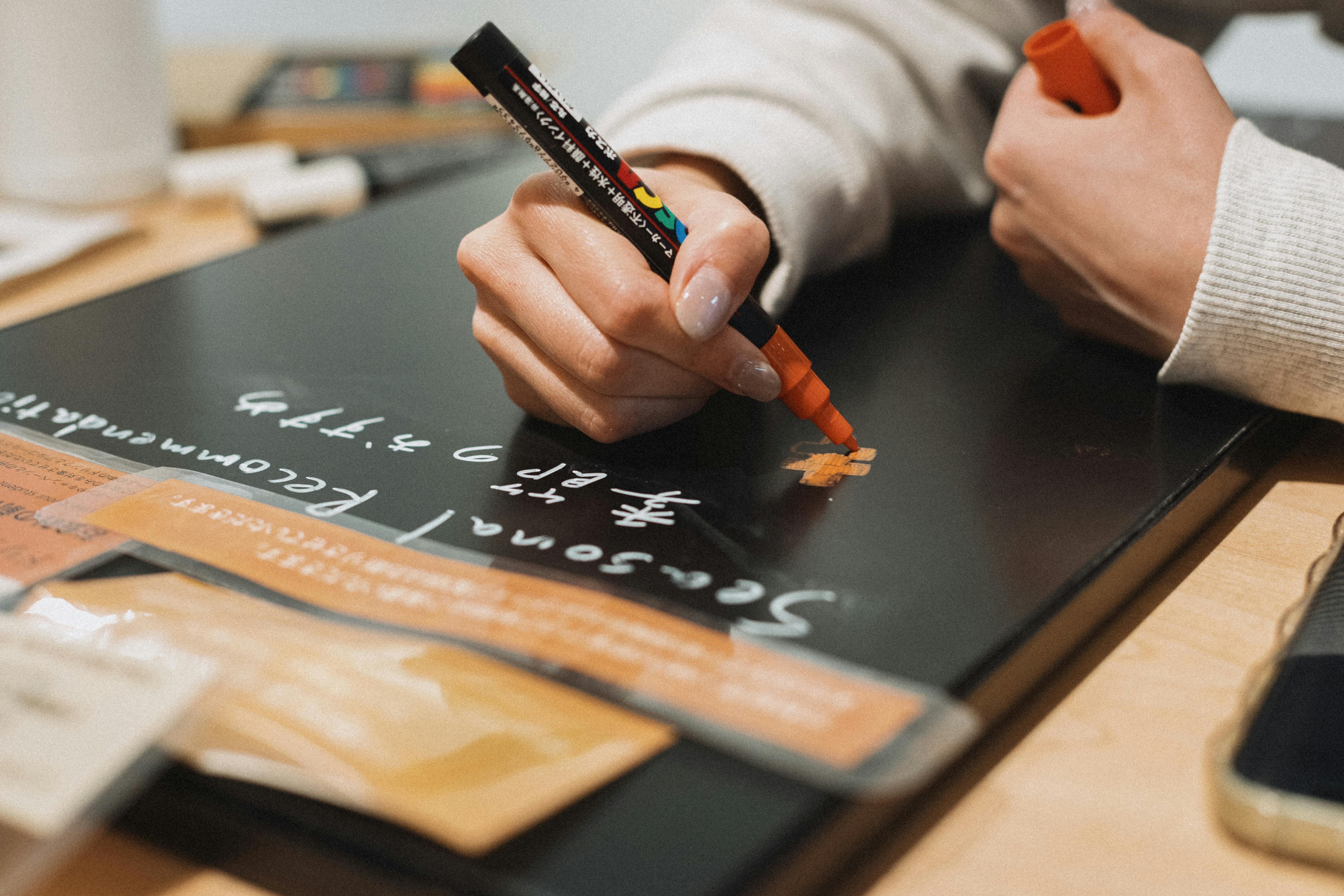 Gratis Una persona scrive con un pennarello su una lavagna nera in un accogliente caffè di Tokyo. Foto a disposizione