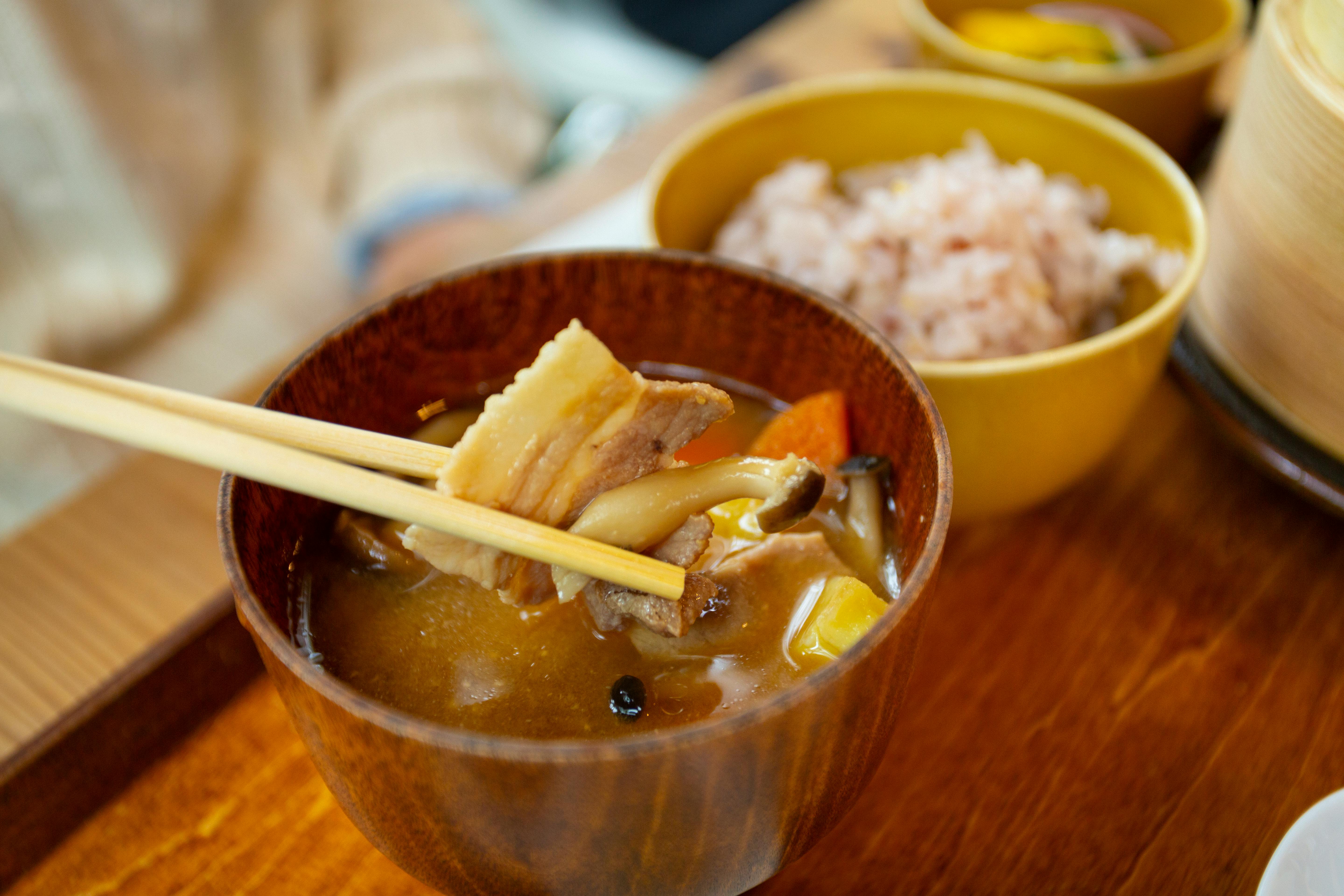 close-up of a jar of miso paste with a wooden spoon, steam rising from a bowl of soup