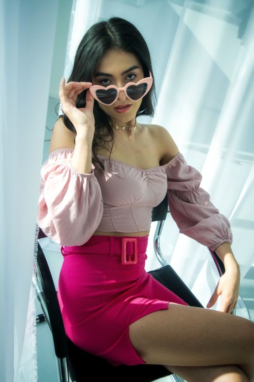 Free Stylish woman in pink outfit wearing heart-shaped sunglasses indoors. Stock Photo
