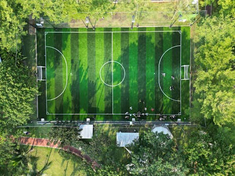 A vibrant green soccer field surrounded by lush trees, viewed from above in Ho Chi Minh City, Vietnam.