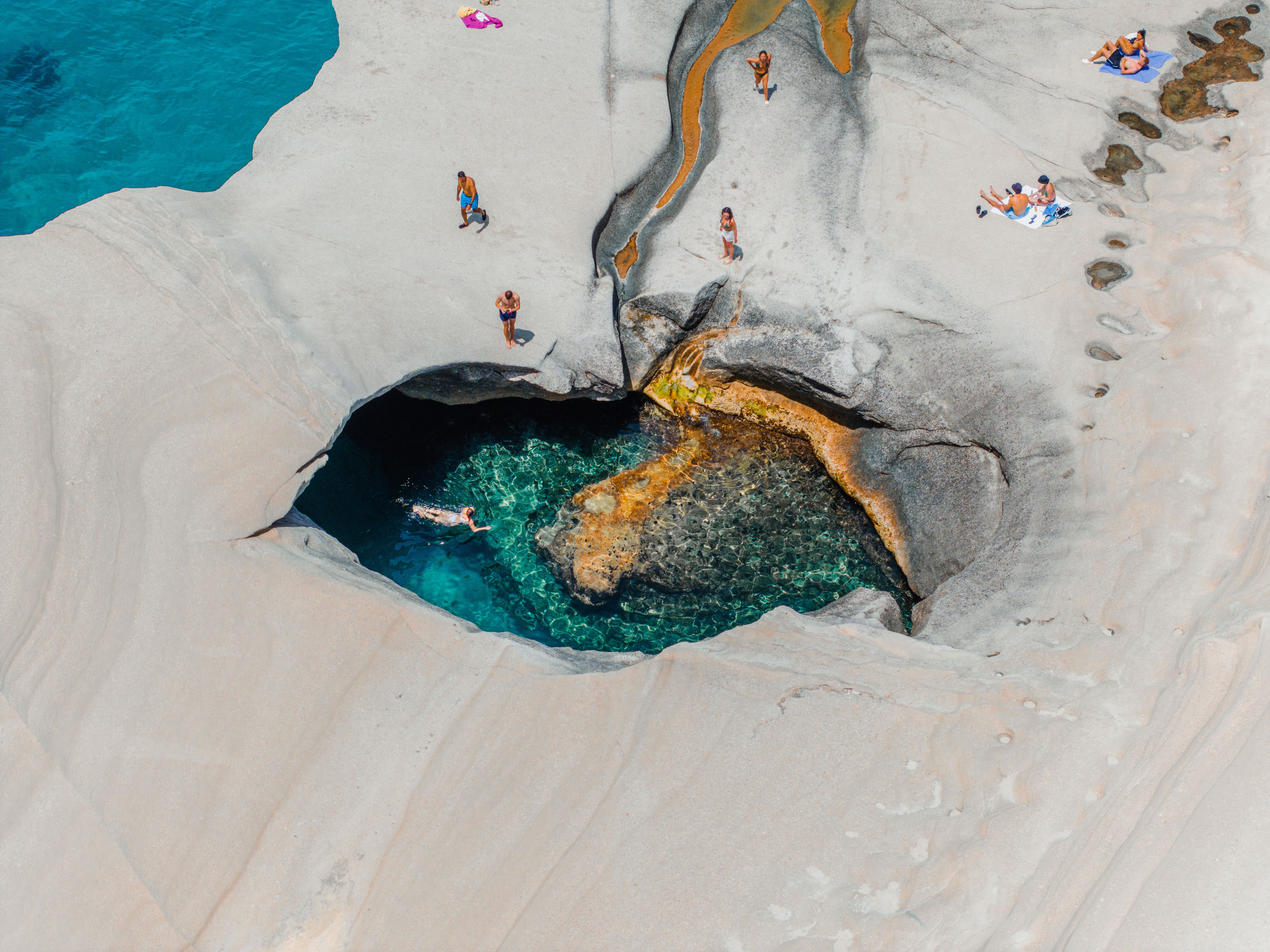 Stunning aerial photograph of a natural rock pool in Milos, Greece, surrounded by sunbathers.