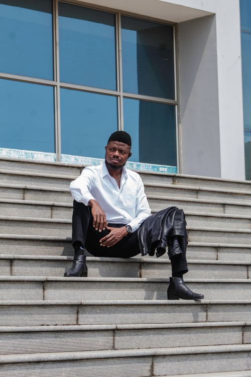 Free Fashionable man in white shirt sitting on stairs outside modern building. Stock Photo