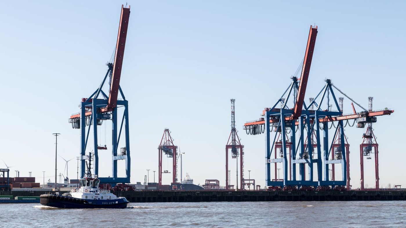 A tugboat passing large container cranes at Hamburg port in daylight