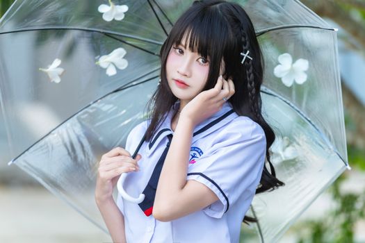 Portrait of a young woman in a school uniform holding a clear umbrella adorned with white flowers.