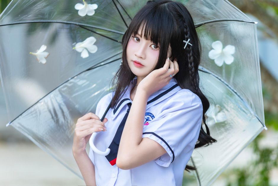 Portrait of a young woman in a school uniform holding a clear umbrella adorned with white flowers.