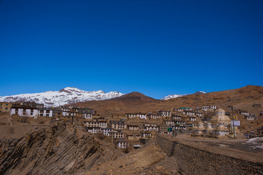 Kibber village nestled in the rugged Spiti Valley with snow-capped mountains under a clear blue sky.