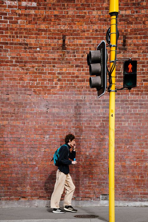 Free A person walks past a red brick wall and traffic light in Wellington, New Zealand. Stock Photo
