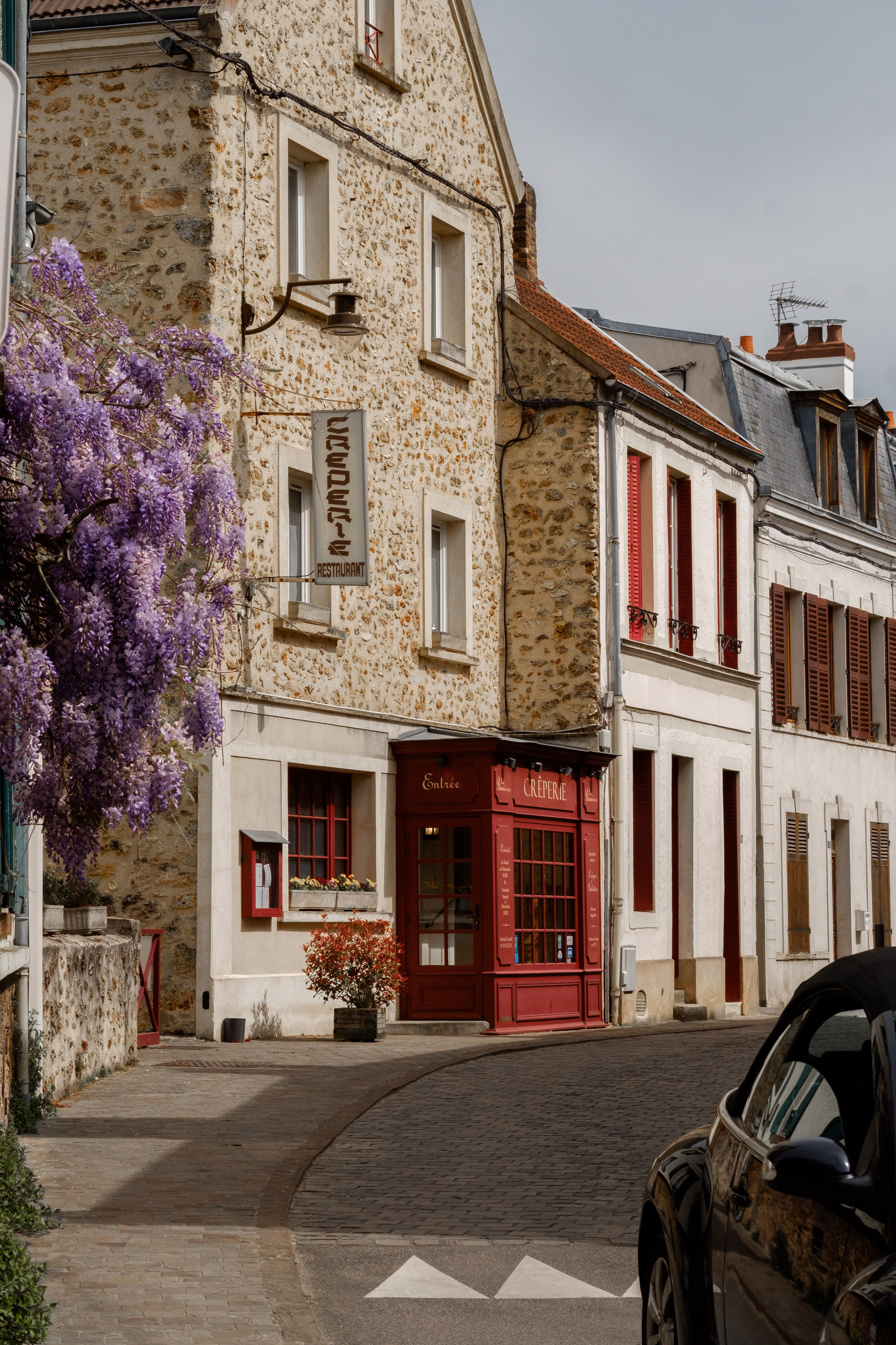 Picturesque view of a quaint Parisian street corner adorned with blooming wisteria and classic stone buildings.