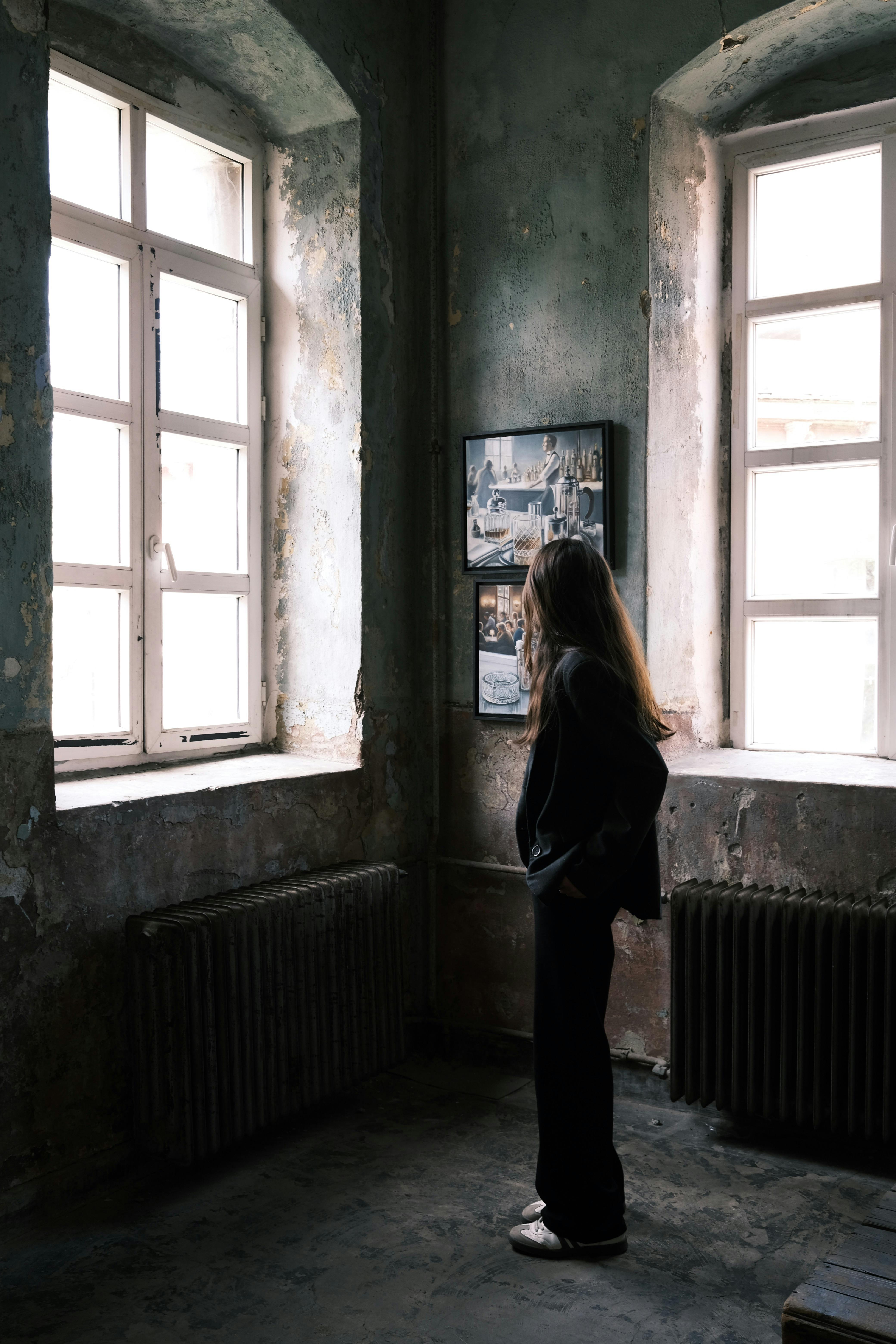 A woman stands thoughtfully by a window in a historic İstanbul building interior.
