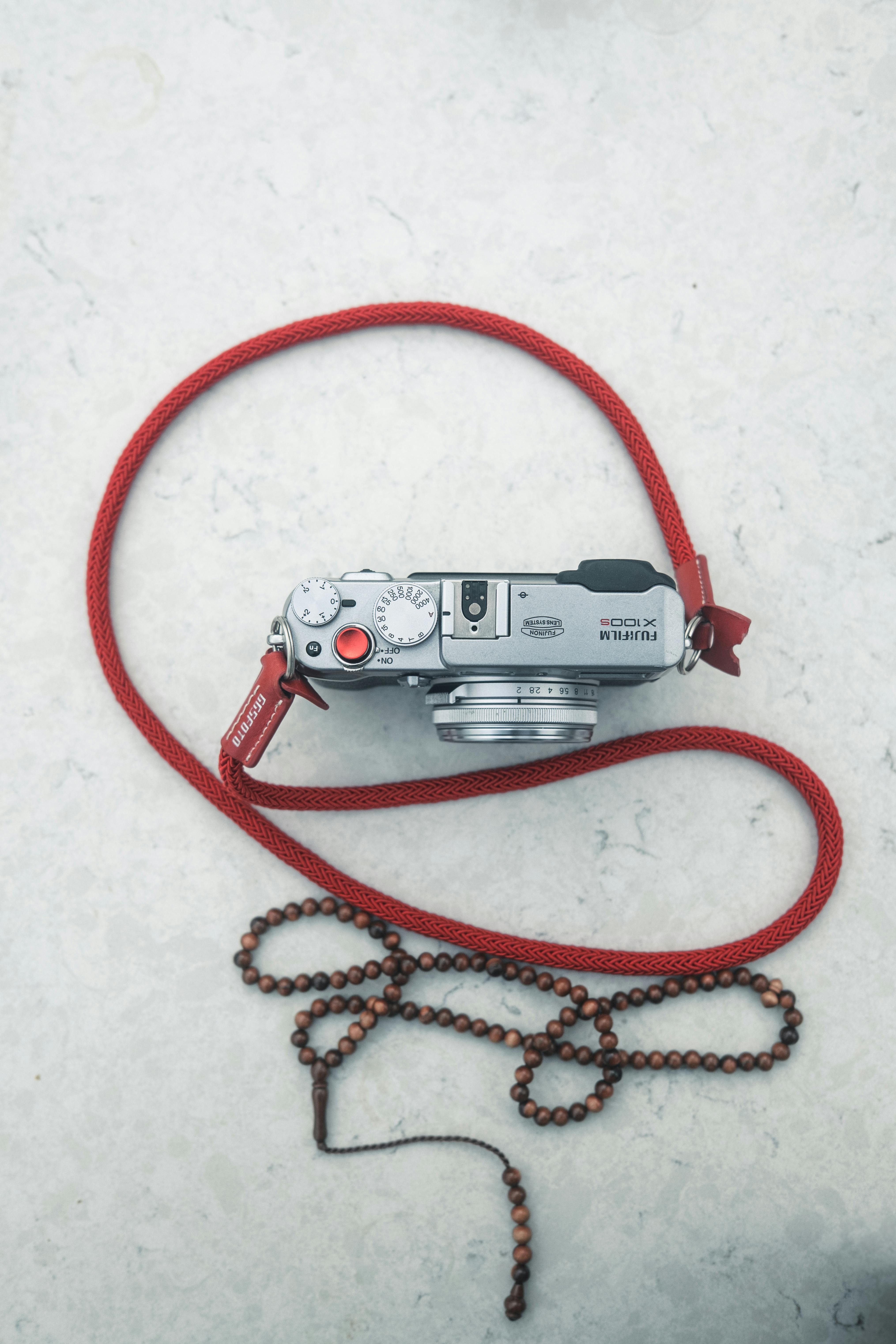Stylový stříbrný fotoaparát s červeným popruhem na mramorovém povrchu, ideální pro nadšence fotografie.